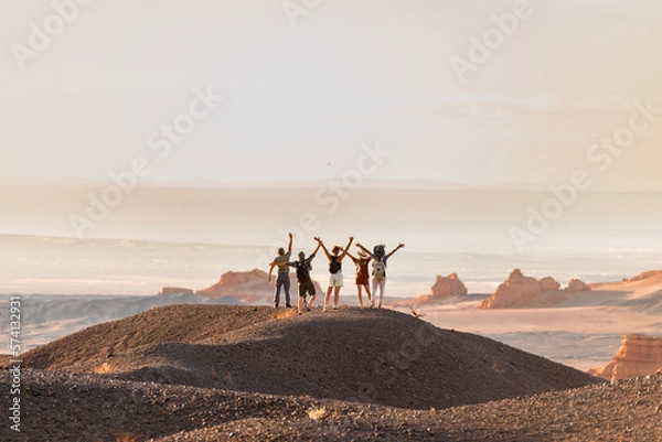 Fototapeta Group of happy tourists stands with open arms at desert view point