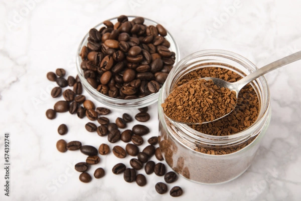 Fototapeta Instant coffee beans in a glass jar on a white marble background. Hot drink ingredients. Instant coffee on the table. Espresso. Place for text. Place to copy. Banner.
