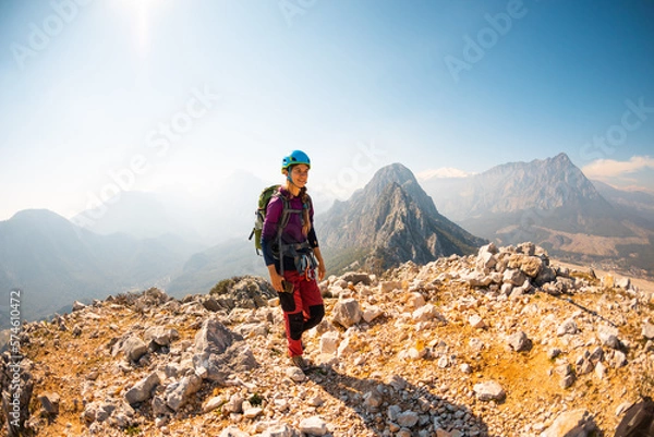 Fototapeta young girl climber in a helmet and with a backpack walks along a mountain range against the backdrop of mountains and climbing and hiking.