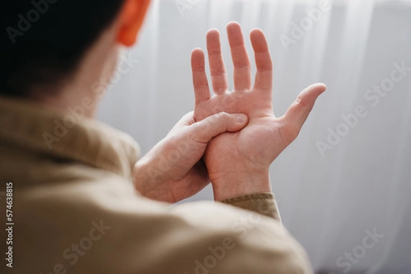 Obraz Close up back view of young man with shaking of Parkinson's disease, symptom of resting tremor, male holding hand to control hands tremor, neurological disorders, brain problems, health care concept