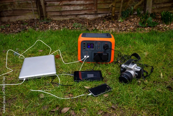 Fototapeta Portable power station solar electricity generator with laptop, tablet and camera charging outdoors.