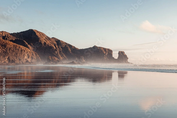 Obraz Piha beach captured at sunset, with the warm colors of the sky reflecting on the tranquil ocean waves.