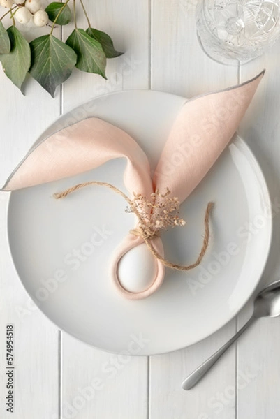 Obraz Easter composition with egg on a white plate on a white wooden table. Easter bunny napkin gift idea wrap egg.