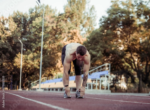 Fototapeta Athletic man with a naked torso practicing stretching exercise before running to the stadium. Healthy lifestyle