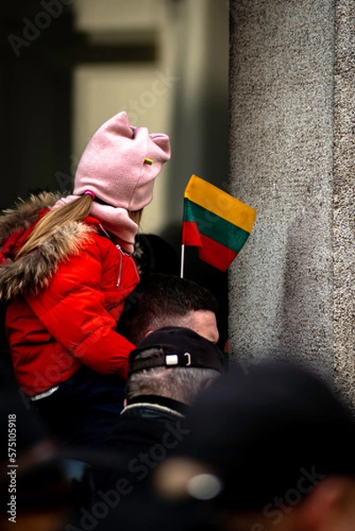 Fototapeta People in Lithuania celebrating their independence day gathered together with Lithuanian flags; a small girl sitting on man shoulders with a flag