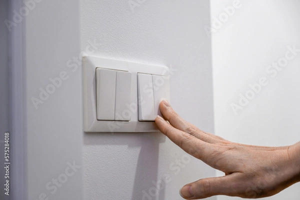 Obraz Close-up of a woman's finger turns on or off a light switch with a white wall at home. Power, energy, electricity saving.