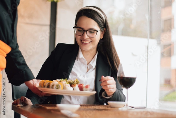 Obraz Smiling woman receiving a plate of sushi from the waiter. Executive woman in a restaurant receiving her order.