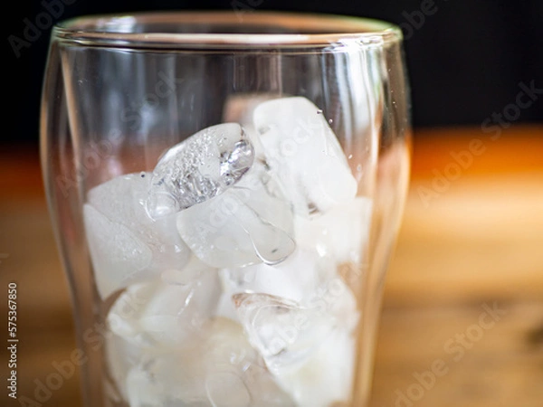 Fototapeta a glass filled with ice on top of a wooden table, black background on background