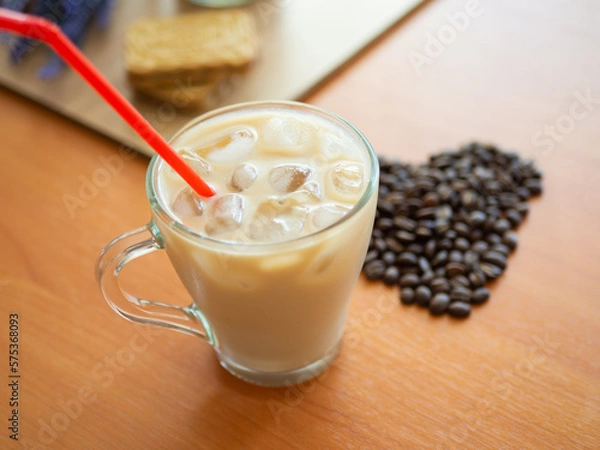 Fototapeta a cup of coffee with ice and a red straw next to a heart shaped pile of coffee beans, cookies on background.