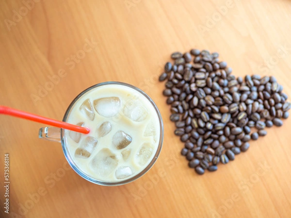 Fototapeta a cup of coffee with ice and a red straw next to a heart shaped pile of coffee beans, cookies on background.Top view