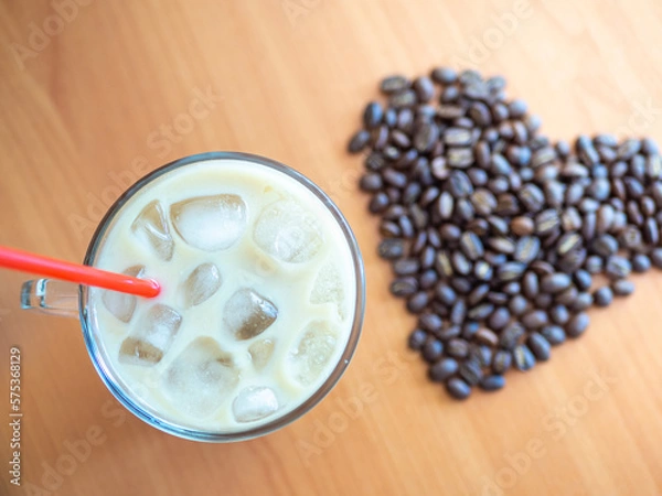 Fototapeta a cup of coffee with ice and a red straw next to a heart shaped pile of coffee beans, cookies on background.Top view