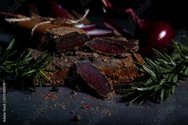Fototapeta Salty, flavorful homemade basturma with aromatic spices and herbs on a dark background. Homemade recipes