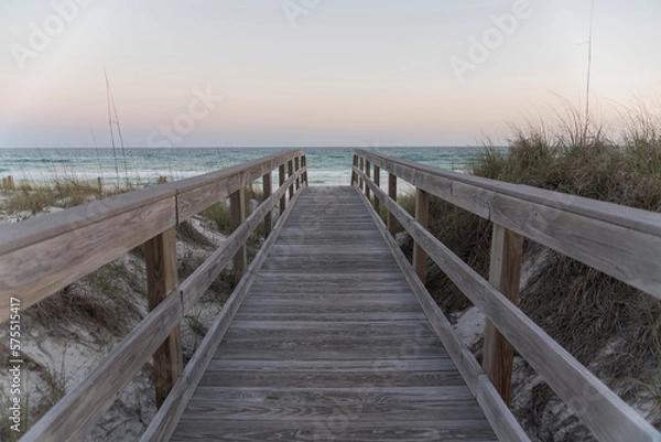 Fototapeta Straight wooden pathway with railings in between sand dunes against the ocean and horizon sky. Wooden walkway near the protected sand dune with grasses with views of ocean waves in Destin, Florida.
