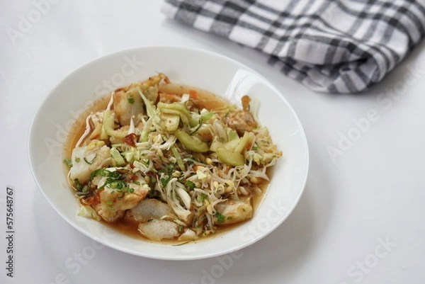 Fototapeta Kupat tahu is a traditional Indonesian food consisting of ketupat and tofu in peanut sauce. Usually include rice cake, tofu, bean sprouts, brown sugar, and prawn crackers. Served in white plate.