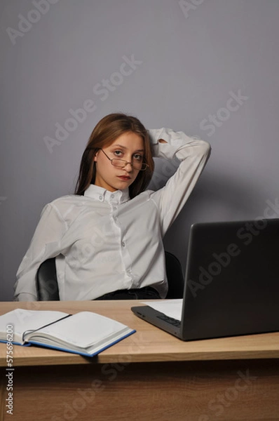 Fototapeta Portrait of an angry business woman sitting near the table and looking at the camera. Grumpiness and work concept