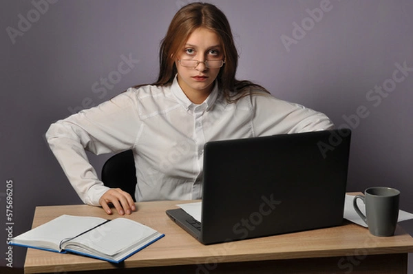Fototapeta Portrait of an angry business woman sitting near the table and looking at the camera. Grumpiness and work concept