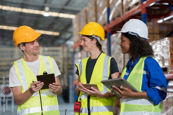 Fototapeta Male and female warehouse workers working and standing talking together at the storage warehouse. Group of warehouse workers discuss and training work in distribution branch