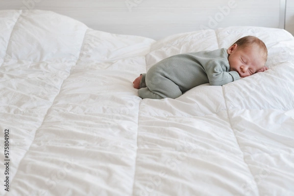 Fototapeta Cute caucasian several days old newborn sleeping on white blanket at home.Adorable,calm, innocent baby indoors.Copy space. Full body shot.Minimalism,lifestyle. 