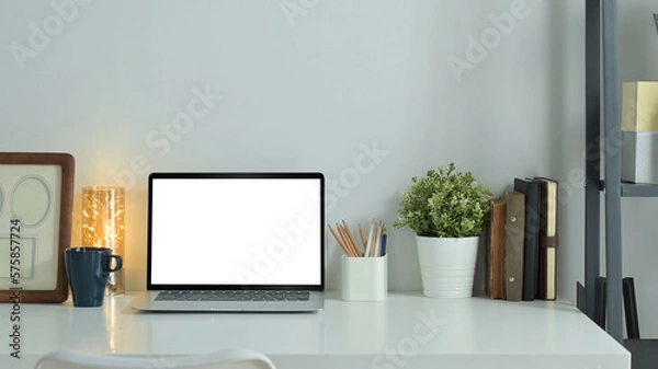 Fototapeta Home office desk with laptop, picture frame and potted plant on white table. Empty screen for text information or content