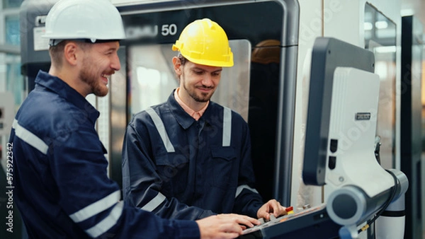 Obraz Two Caucasian production engineers in safety wear are discussing to plan for operating CNC machine in the factory. Male factory workers are controlling the process of production during work hours.
