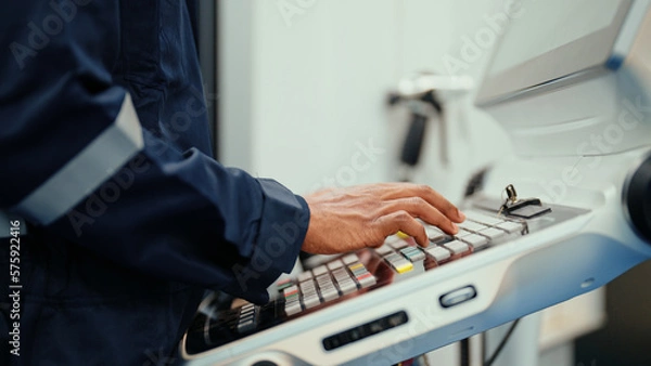 Obraz Close-up of Caucasian production engineer's hand with safety wear operating CNC machine in the factory. A male factory worker is programming industrial machine to control the process of production.