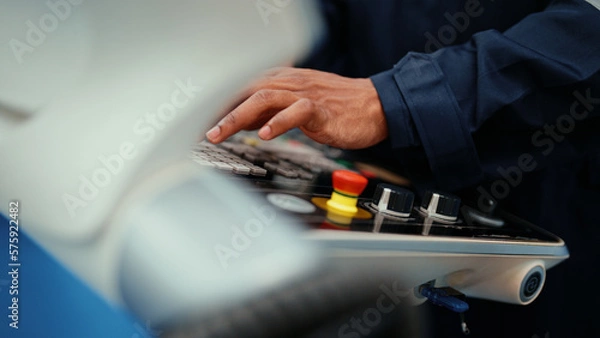 Obraz Close-up of African production engineer's hand with safety wear operating CNC machine in the factory. A male factory worker is programming and adjusting industrial machine to control the production.