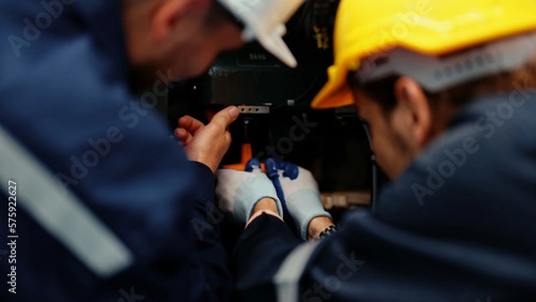 Obraz Close-up of two Caucasian production engineers in safety wear assisting in adjusting and maintaining CNC machine in the factory. Male factory workers are examining the industrial machine to fix it.