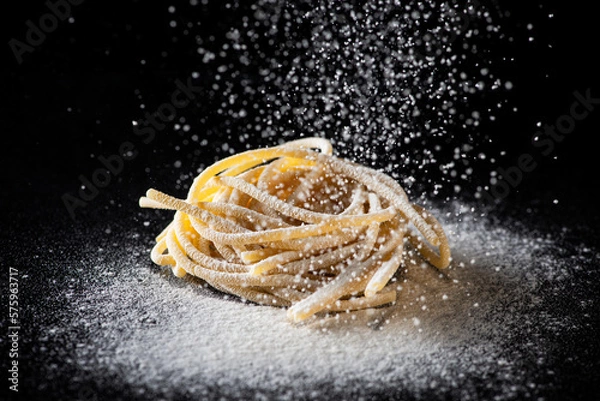Obraz Uncooked traditional hand - rolled durum wheat pasta Pici of Tuscany, black background, macro photo of pasta pici and selective focus with white flour falling down