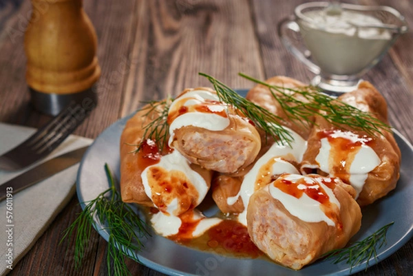 Fototapeta Cabbage rolls poured with sour cream and sauce lie in a small gray plate, which stands on a dark wooden table.