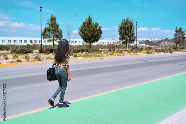 Fototapeta Woman walking on the street with black bag and trees in the background.