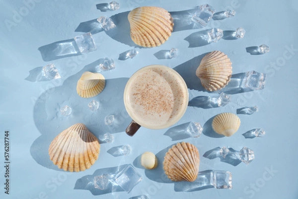 Fototapeta Cup of coffee with sea shells, ice, water drops on the blue background. Coffee latte with seashells in the middle of the table. Coffee break on  island. Happy day, morning. Enjoying vacation.