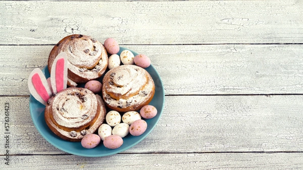 Fototapeta Easter eggs and decor on fresh buns with spirals with white icing sugar.