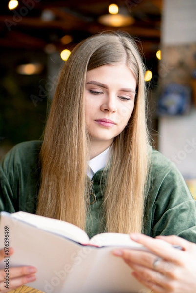 Obraz A girl is reading a book in a cafe. The student is studying scientific literature.