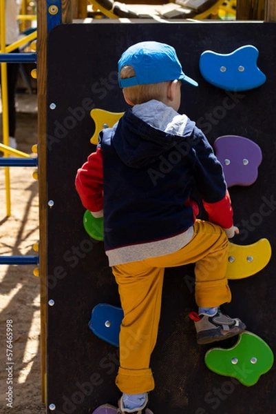 Fototapeta boy toddler climbing on the outdoor climbing wall in the playground