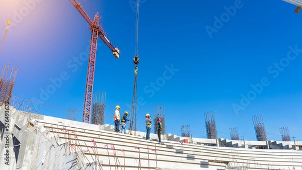 Fototapeta A crane lends a hand to Latino workers who are building a stadium step by step. The metal skeleton of the stadium awaits its completion.