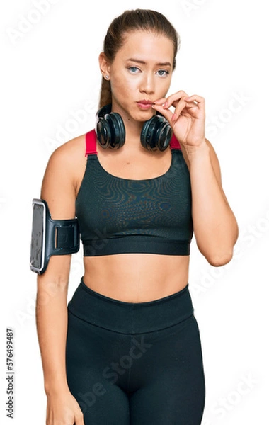 Fototapeta Beautiful blonde woman wearing gym clothes and using headphones mouth and lips shut as zip with fingers. secret and silent, taboo talking