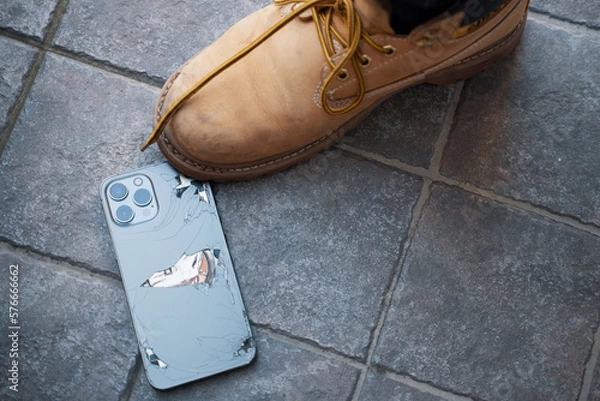 Obraz Broken back glass of smartphone fallen on ground. Shoe stepping on smartphone.