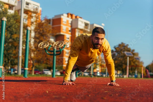 Fototapeta Male athlete exercising in the park doing push-ups and focused on working on his upper body