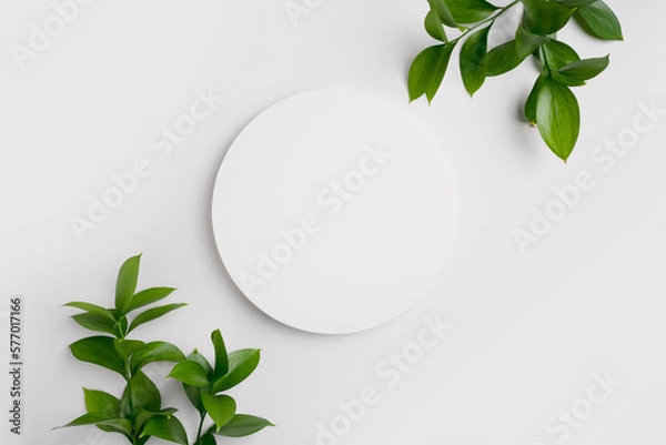 Fototapeta Empty round podium and green leaves on light grey background top view. Pedestal and fresh natural branches for cosmetic advertising. Eco product presentation mockup. Top view. Minimal flat lay.