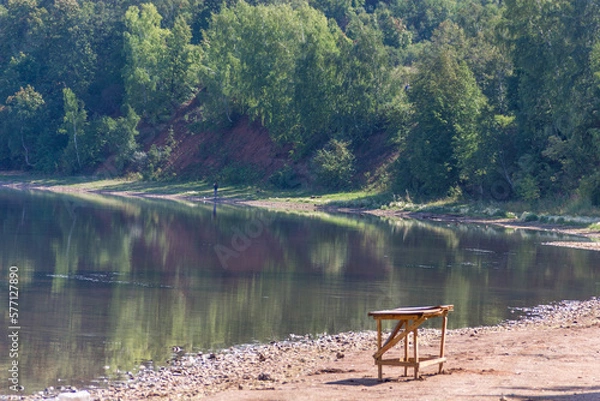 Fototapeta a wood table sitting on the shore of a lake, green forest on background