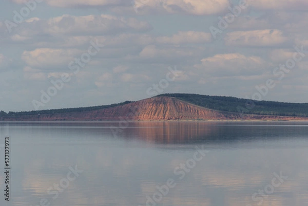 Fototapeta lake with clouds in the sky, red hill with forests on background. hill symmetric reflection in the water