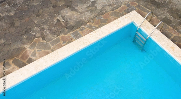 Fototapeta Aerial closeup of a rectangular swimming pool with ladder, belonging to a large villa. The pool is empty and no one is swimming. Around the water there is a stone floor.
