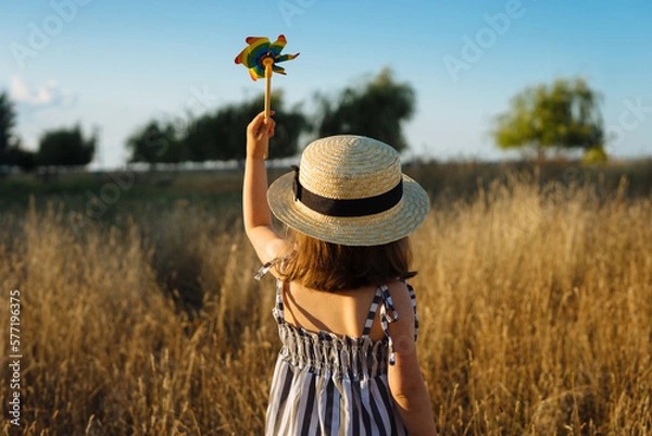Fototapeta Little girl holding up a pinwheel toy against clear sky in the meadow
