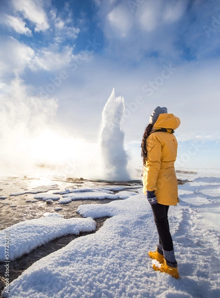 Fototapeta A girl standing in front of Famous Geysir in Iceland in beautiful sunrise light. One of the most famous natural heritage on Iceland.