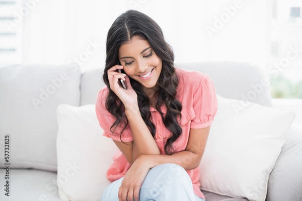 Obraz Smiling cute brunette sitting on couch phoning