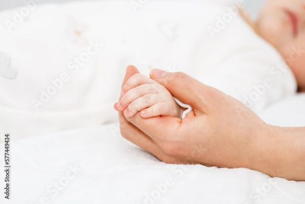 Fototapeta Close up mother holding tiny hand of little newborn baby boy girl, helping hands, bonding different generations. Happy motherhood concept.