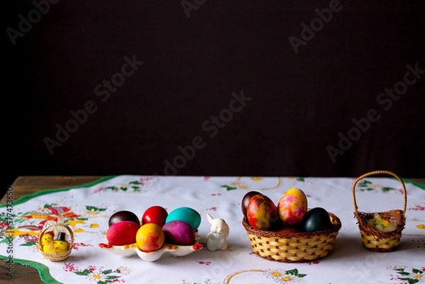 Obraz Colored easter eggs in a wooden basket at a white tablecloth on a black background