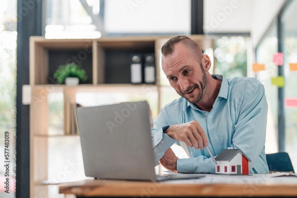 Fototapeta Professional and smart Caucasian male engineer having an online meeting with his team, explaining the building plan and design, working in the office.