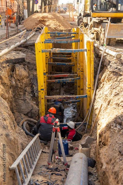 Obraz Workers working at deepening supported by trench box with pipe bedding pea gravel during installation of drainage pipe.