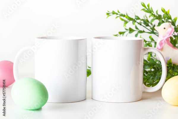 Fototapeta Easter mockup of two white mugs on table with colorful painted eggs and greenery. Blank coffee cups mock up.